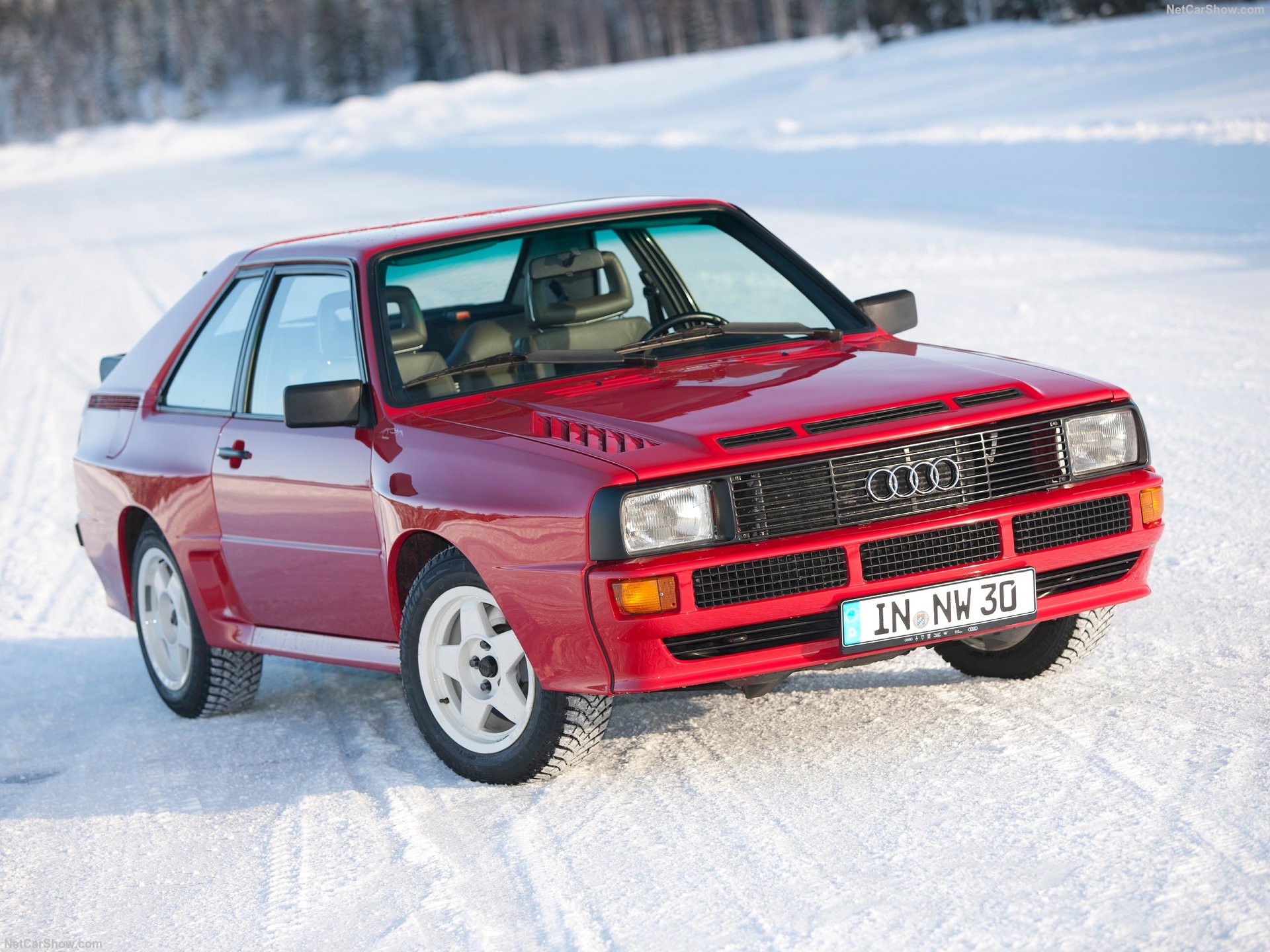 Three-quarter front view of a 1984 red Audi Sport Quattro driving on snow