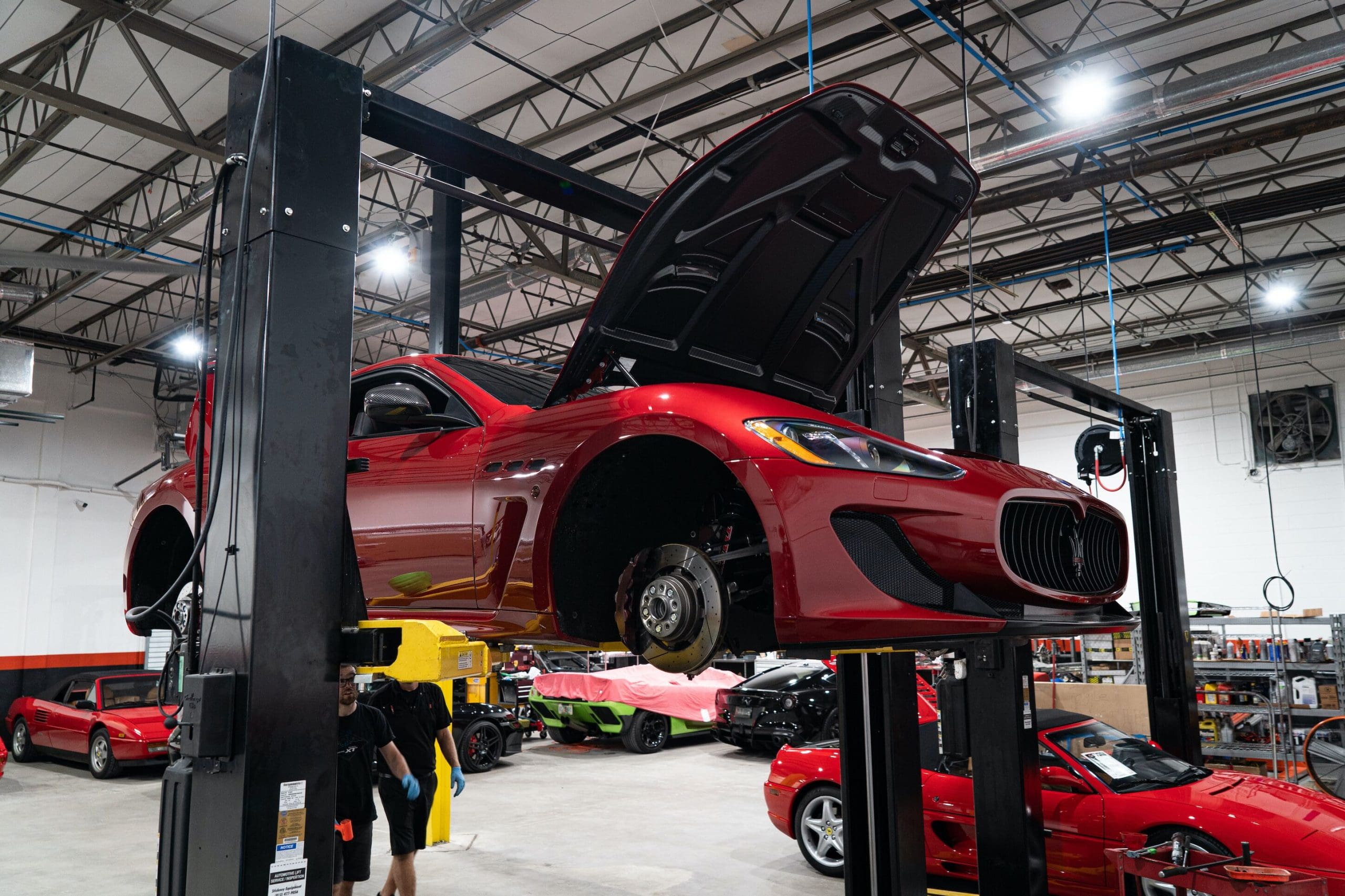 Three-quarter front view of a red Maserati Gran Turismo Coupe lifted at a repair shop