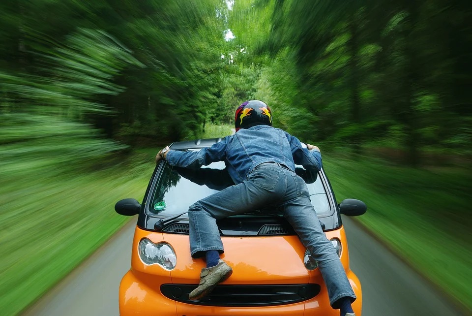 Man climbing on hood of moving car