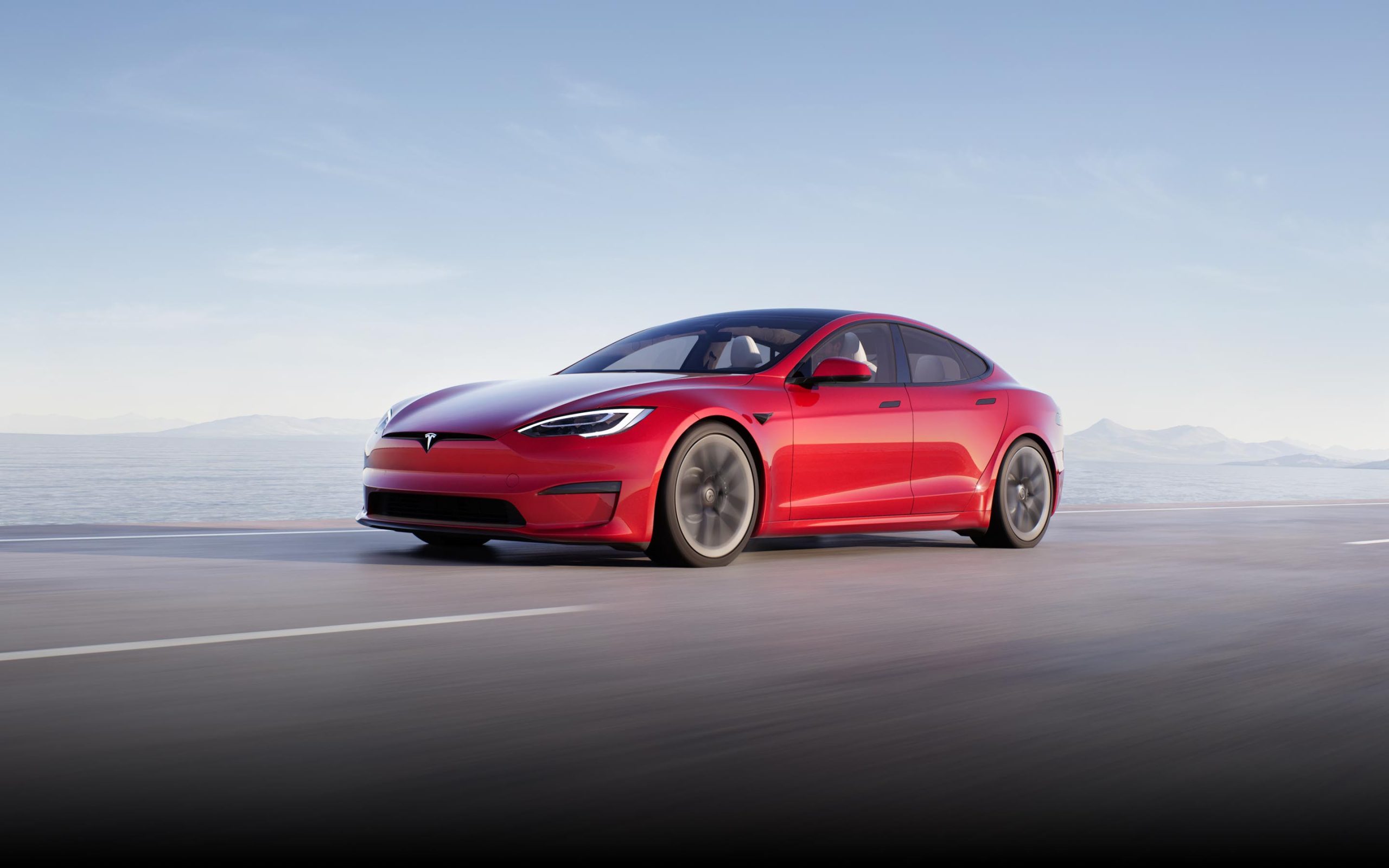 A side view of the Tesla Model S Plaid driving on a road with blue sky in the background