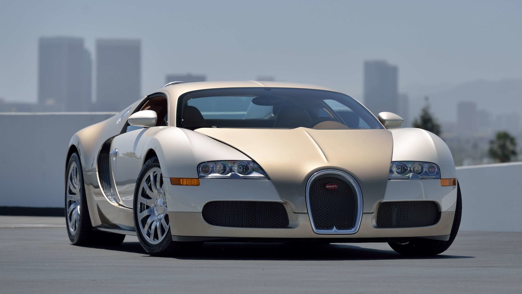 Gold and white Bugatti Veyron on city street with skyscrapers in background