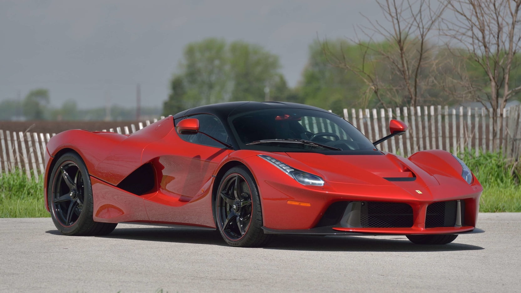 Bright red Ferrari LaFerrari on road with white fence and trees in background