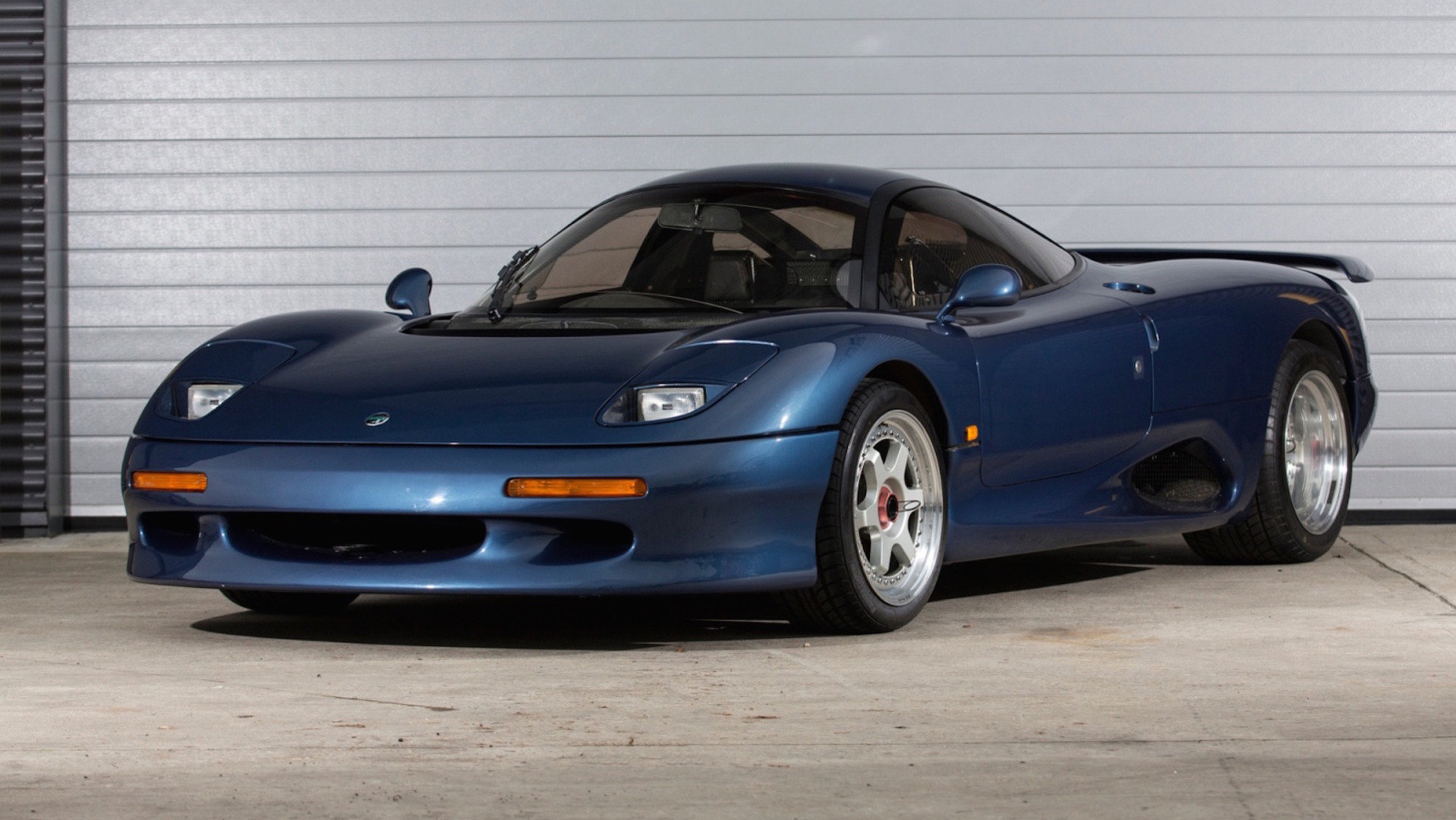 Navy Jaguar XJR-15 sitting on tarmac outside garage