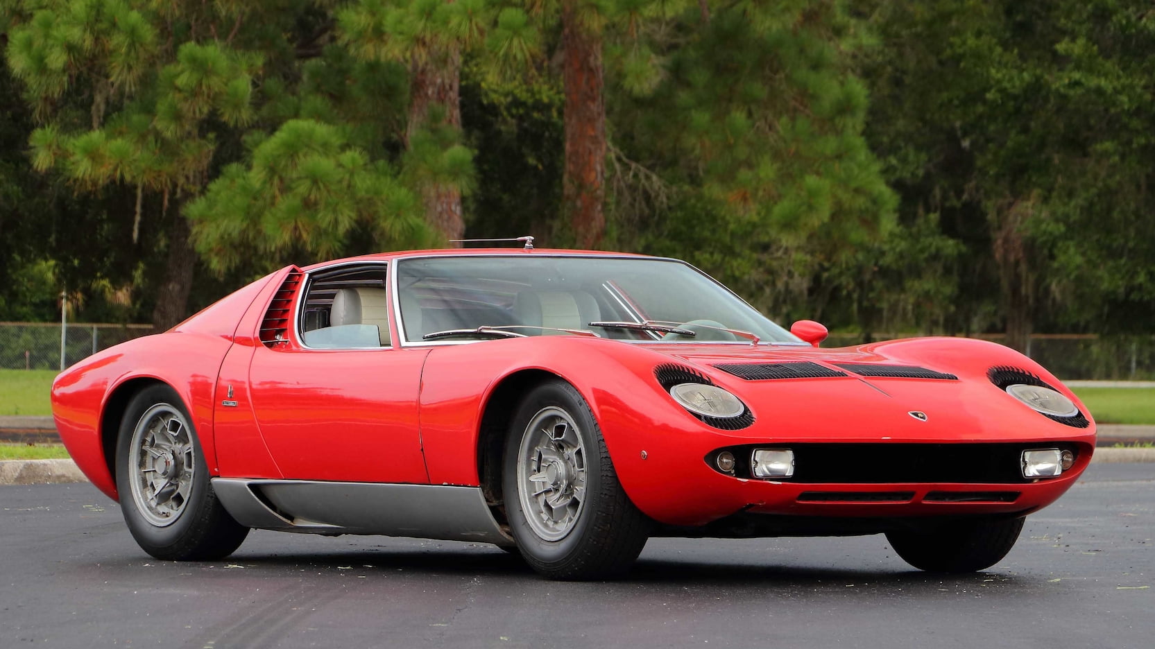 Bright red Lamborghini Miura sitting on road with trees in background