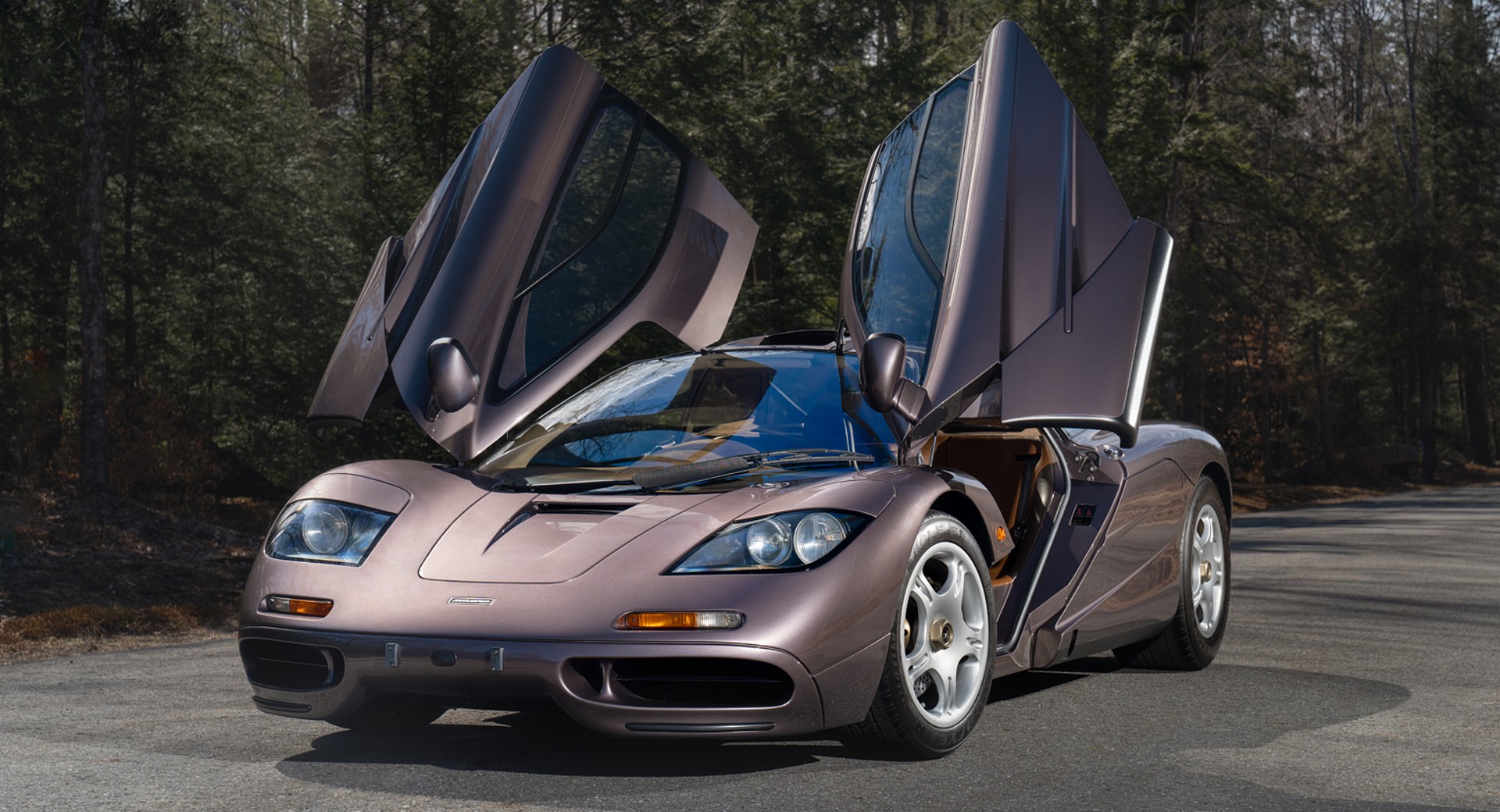 Grey McLaren F1 sitting on road in forest with doors open