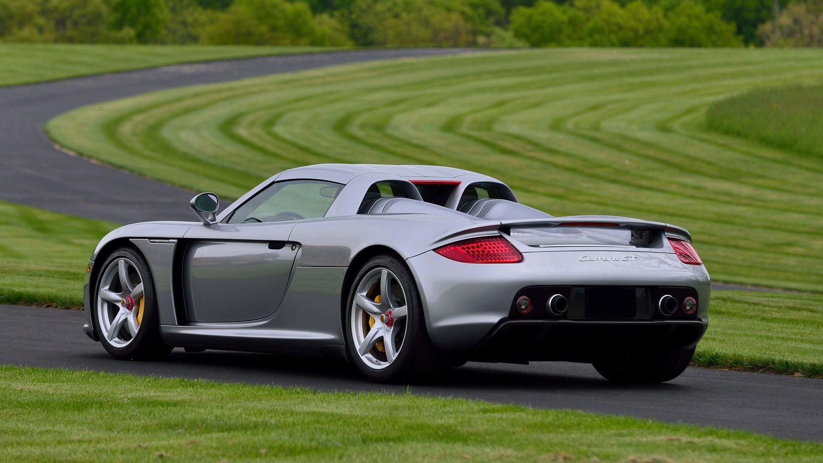 Grey Porsche Carrera GT on road cutting through grassy field