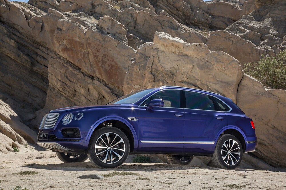 Blue Bentley Bentayga parked in desert near rock wall