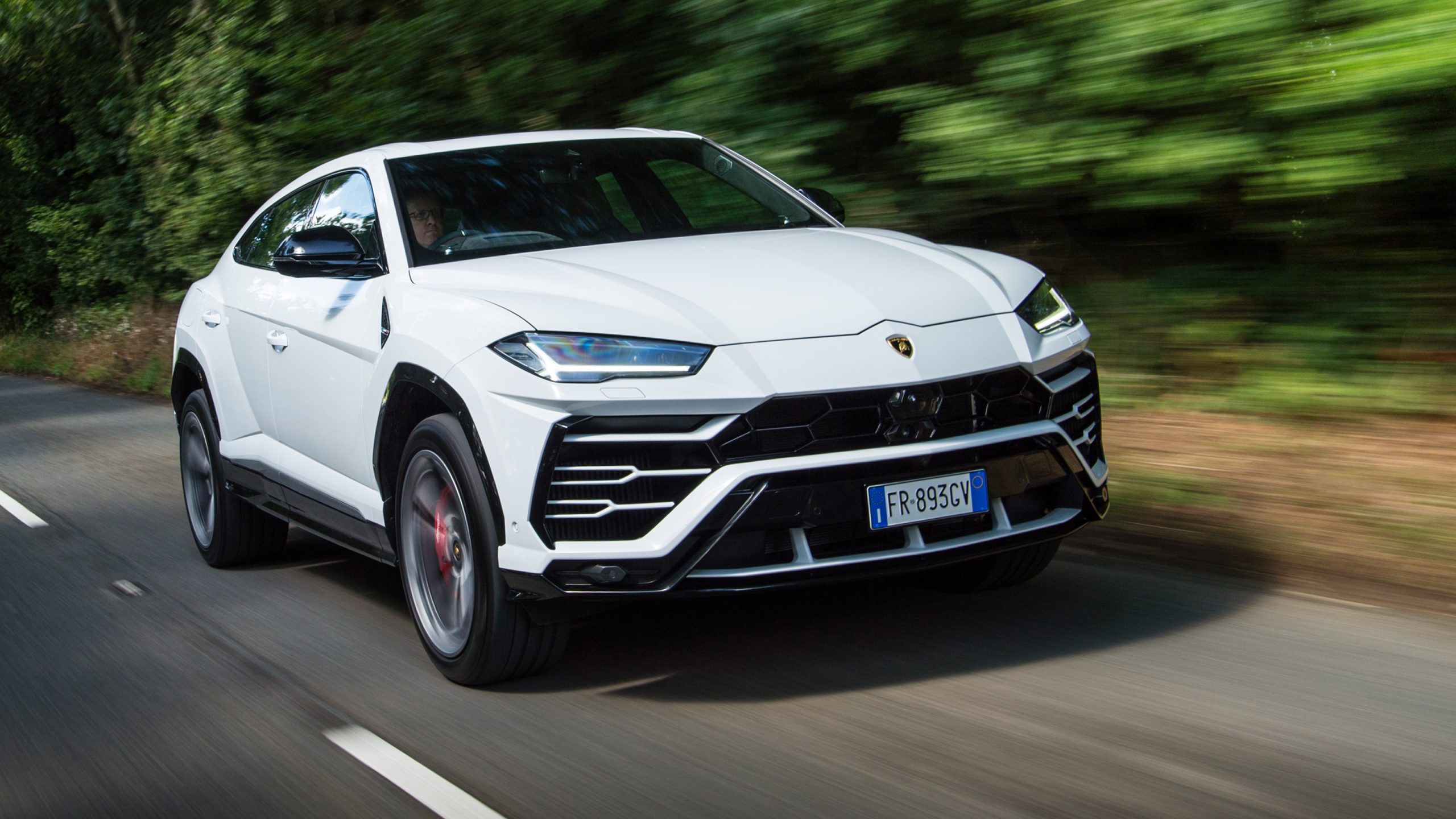 White Lamborghini Urus speeding down road with trees