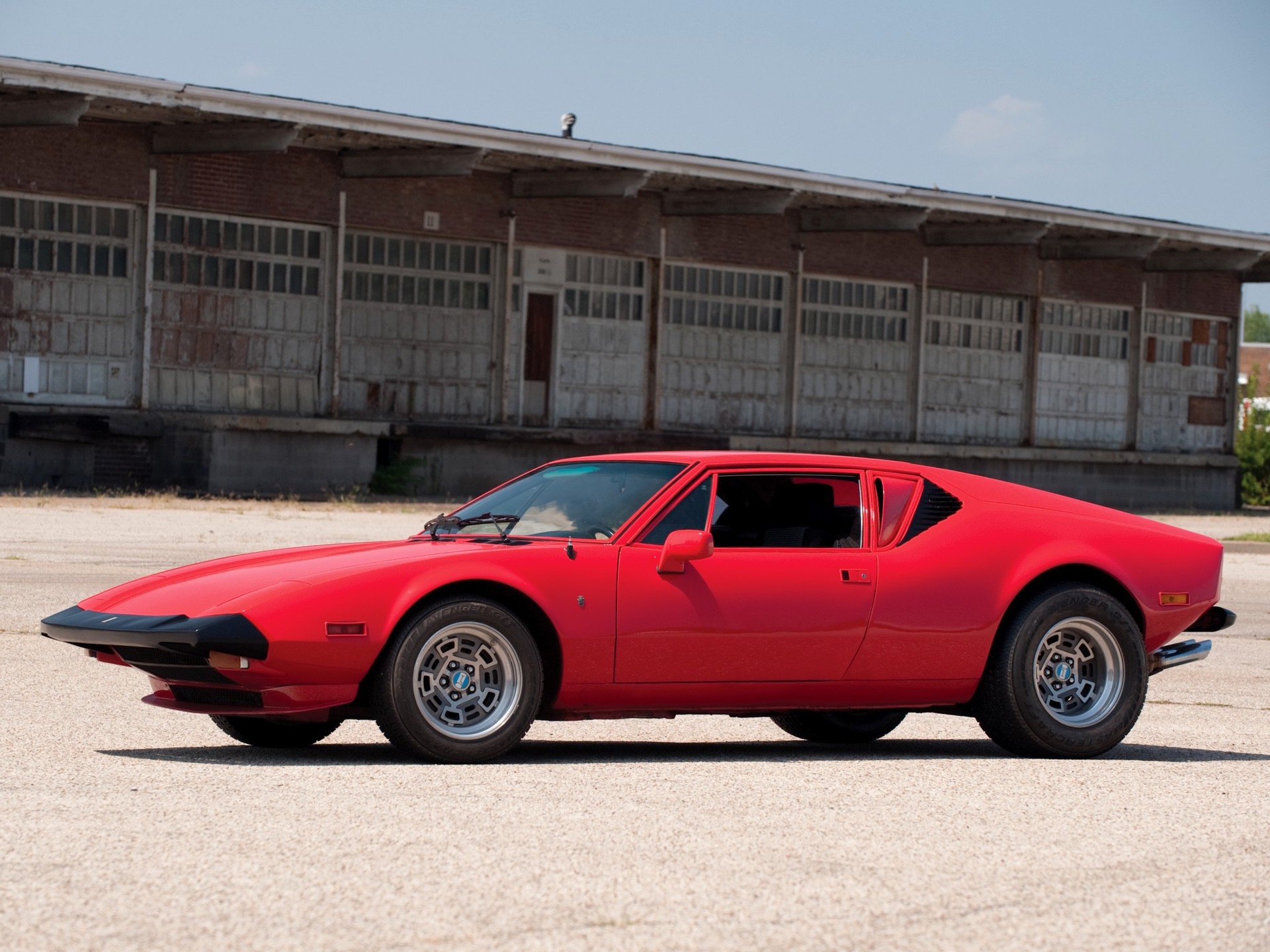 Red DeTomaso Pantera parked on ground in front of building