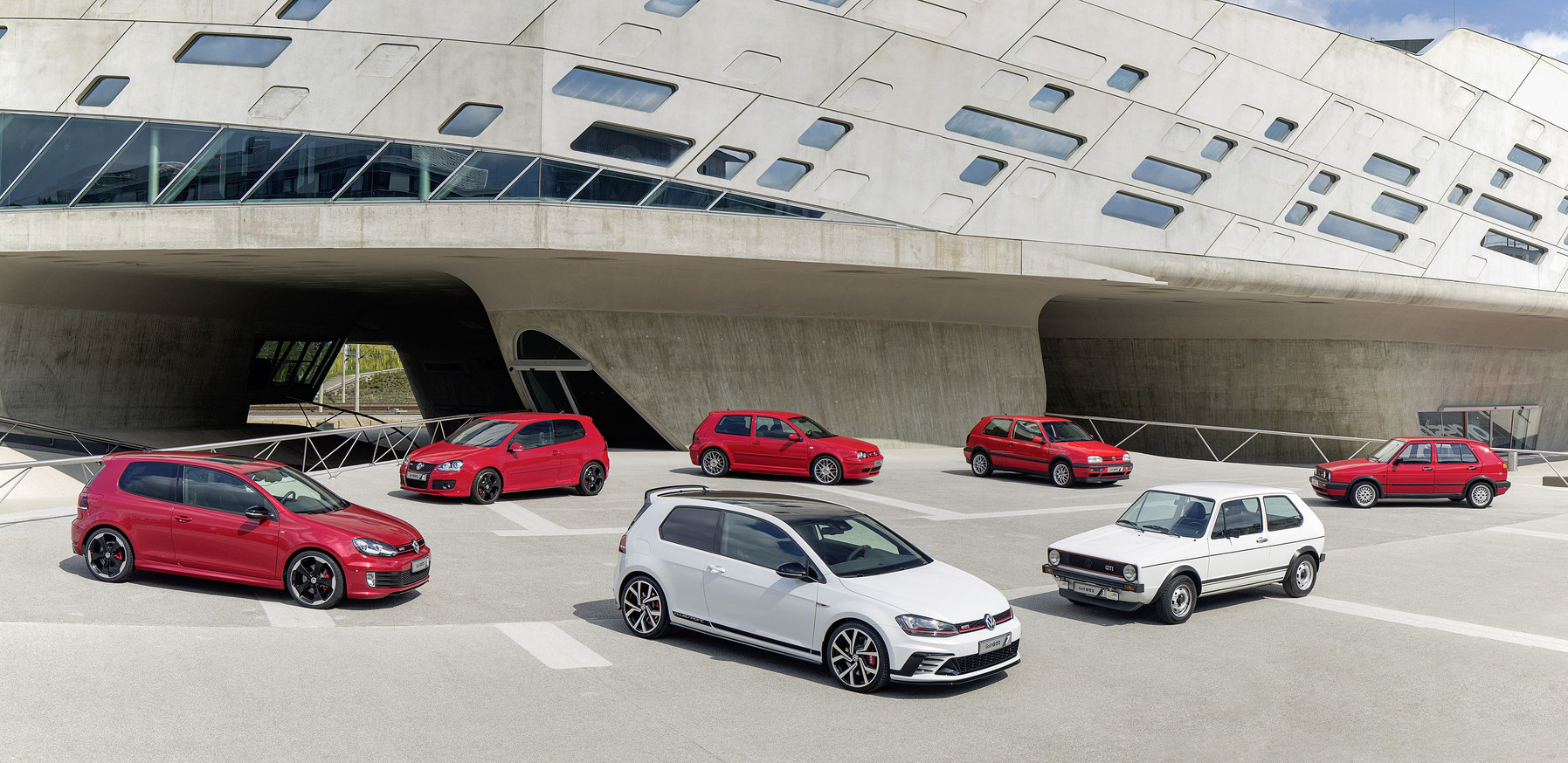 Red and white Volkswagen Golf GTI cars parked in front of modern building