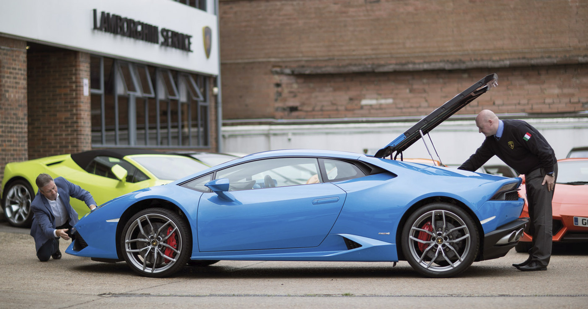 Man inspecting the engine bay of a blue Lamborghini Huracan