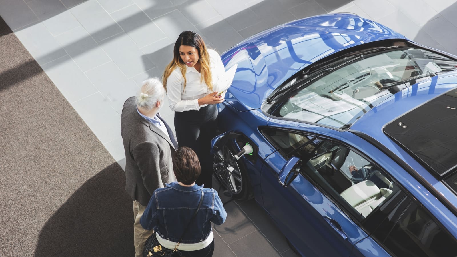 Woman selling blue car to two people