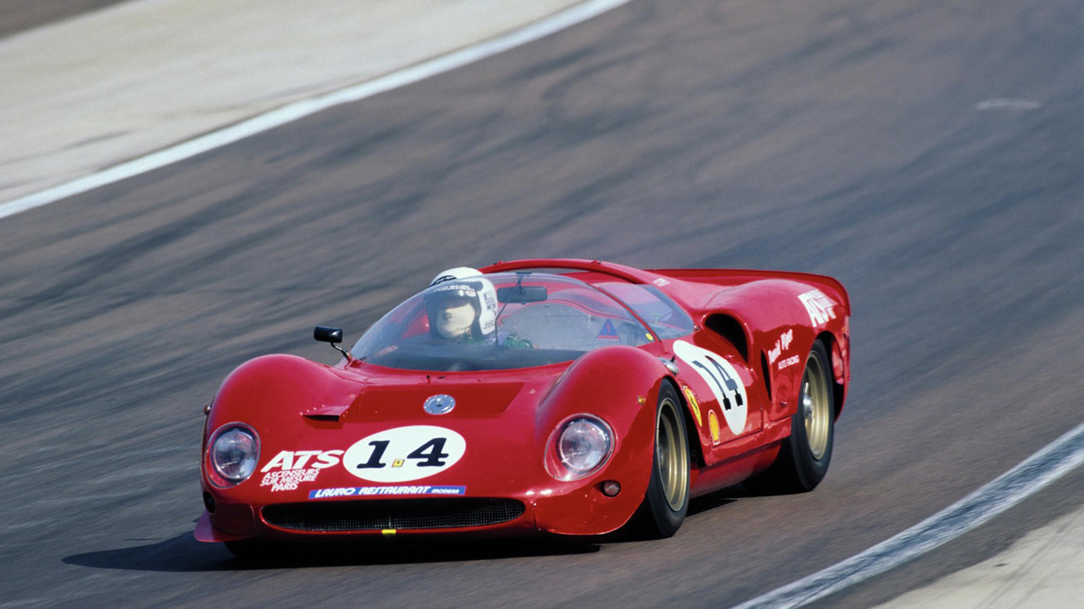 Front-angled shot of a Ferrari 330 P2 driving at speed on a racetrack.