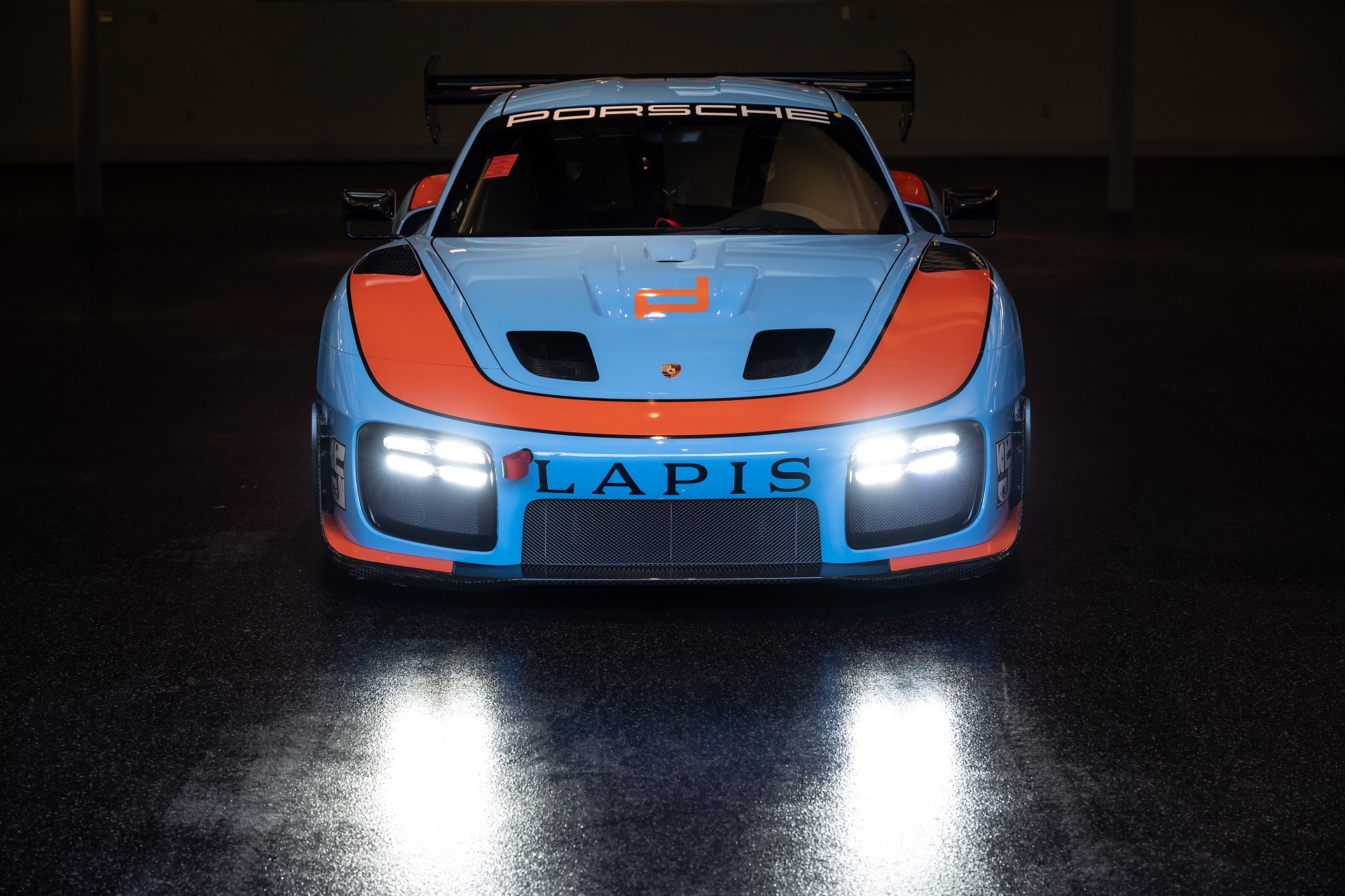 frontal view of a Gulf-liveried 2019 Porsche 935 with lights on.