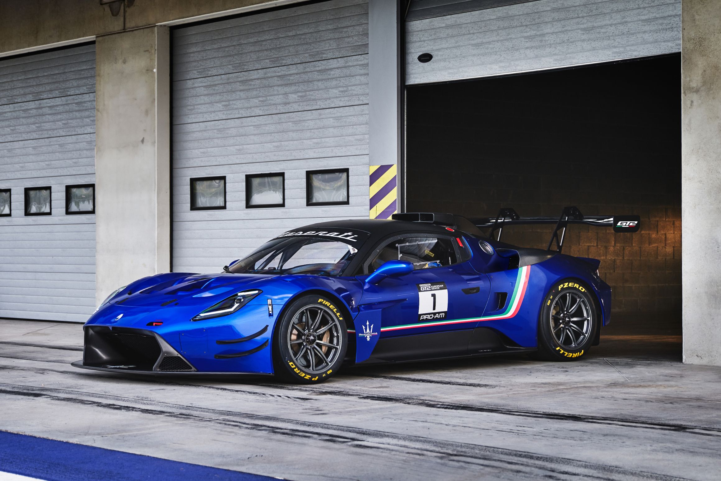 Front-angled view of a blue Maserati GT2 race car parked outside a garage on the pit lane.