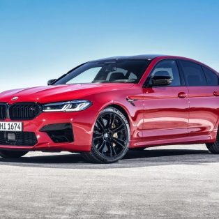 Front-angled view of a 2021 BMW M5 Competition finished in a bold red colour with orange undertones.
