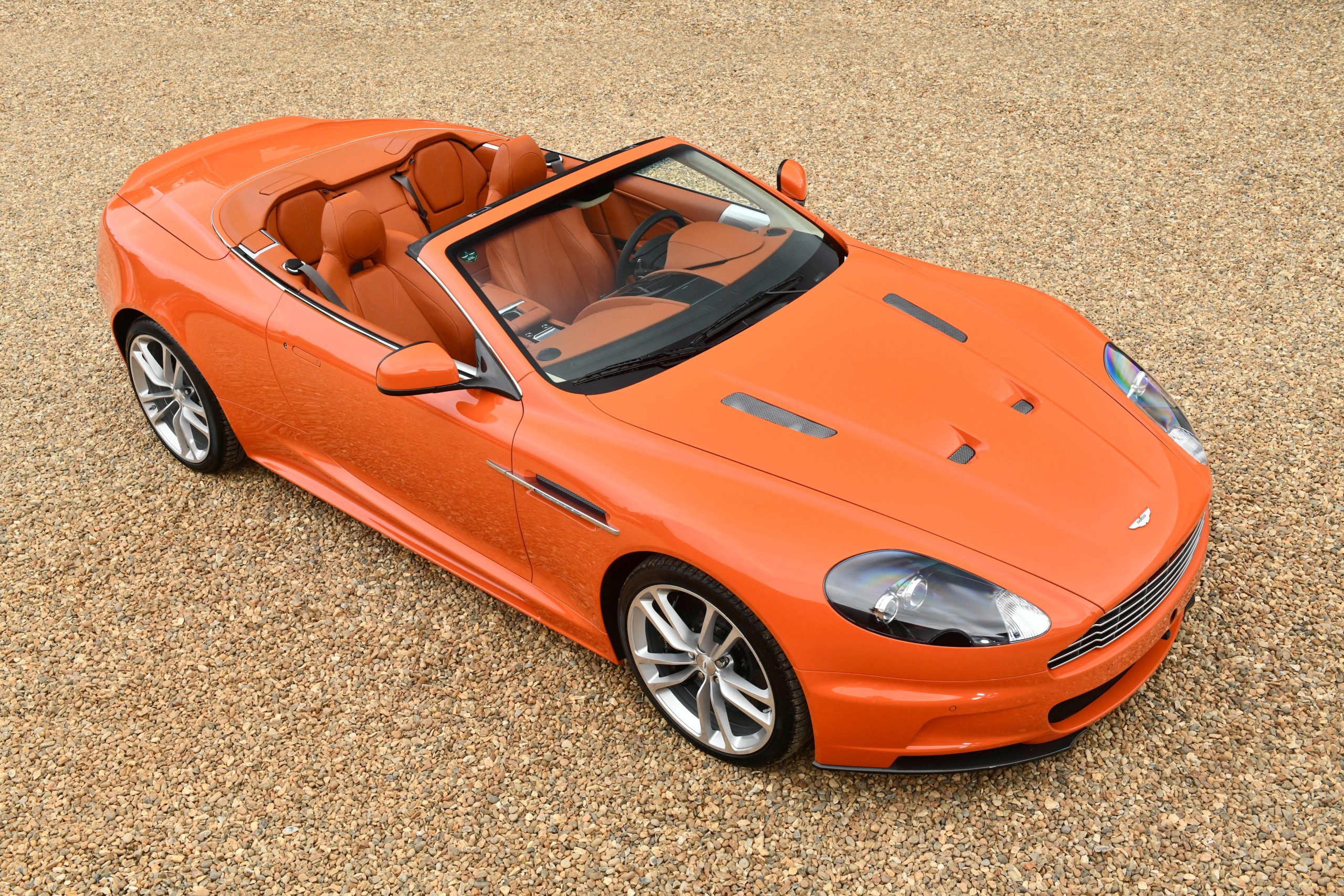 Angled aerial view of an orange Aston Martin DBS Volante