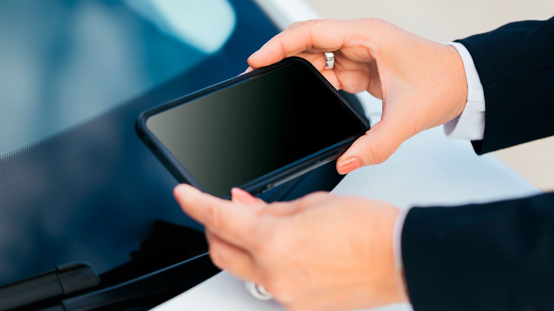 Person using smartphone to check vehicle VIN number near car windshield